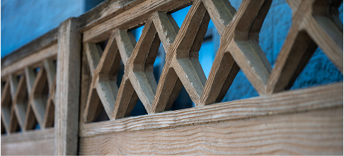 Close-up of a wooden fence with a repeating diamond-shaped pattern, set against a blue background.