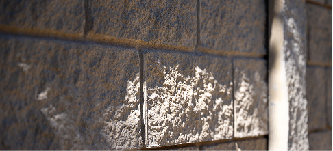 Close-up of a textured brick wall with sunlight casting shadows and illuminating part of the surface, highlighting the rough and uneven texture of the bricks.