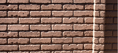 A close-up view of a textured brick wall with a corner edge, showing uneven surfaces and rough brick patterns in shades of brown.