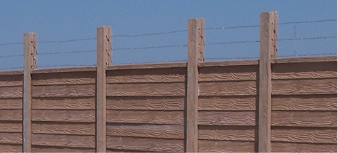 A close-up view of a wooden fence with vertical posts and horizontal planks, topped with barbed wire, set against a clear blue sky.