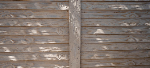 Beige wooden fence with horizontal panels and a vertical support in the center, featuring textured lines and dappled sunlight creating patches of shadow across the surface.