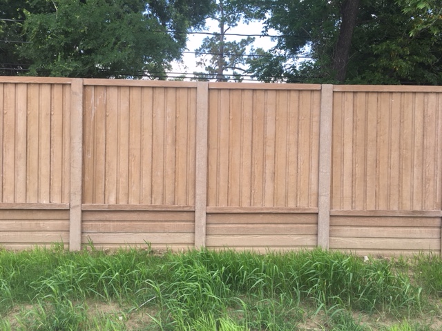 A tall wooden fence with vertical planks stands behind a patch of green grass, with leafy trees and power lines visible in the background.
