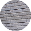 A circular image showing a close-up view of a gray brick wall with visible mortar lines and some imperfections on the brick surfaces.
