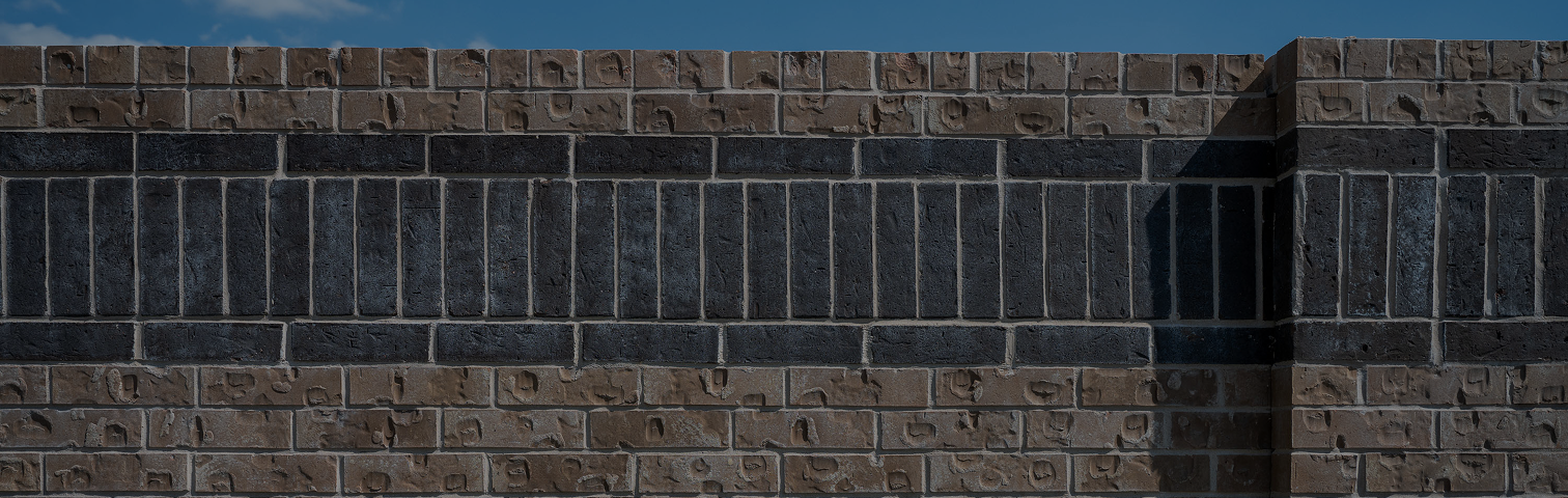 A close-up view of a brick wall with alternating rows of brown and dark gray bricks, under a clear blue sky. The brick pattern is symmetrical and features both horizontal and vertical alignment.