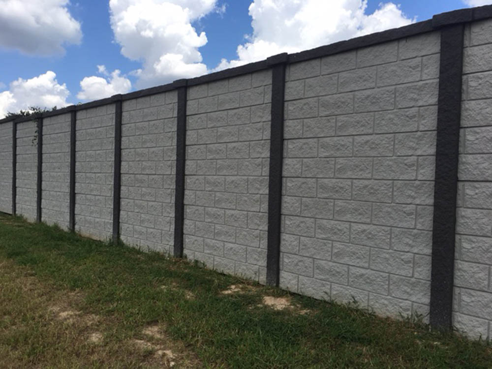A tall concrete block wall with vertical dark columns, standing on grassy ground under a partly cloudy sky.