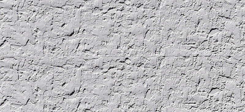 Rough gray stucco wall texture with irregular patterns and small cracks running horizontally across the surface. The wall has a rugged, uneven appearance, typical of exterior plaster finishes.
