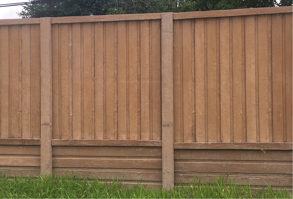 A tall wooden fence with vertical slats and horizontal baseboards stands behind green grass, with trees and a power line visible above it.